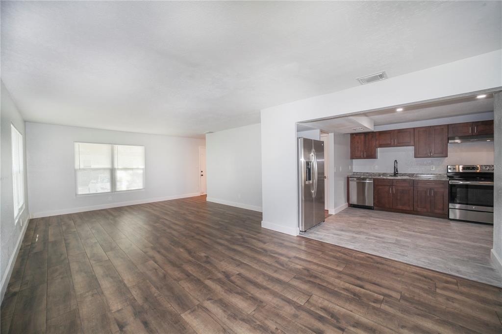 A living room with wood-look flooring opens into a kitchen featuring dark cabinets and appliances — 331 AMHERST AVENUE UNIT 56, SARASOTA, FL