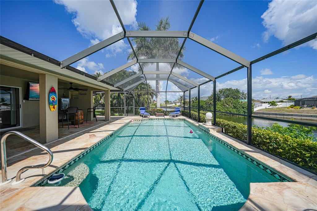 A screened-in swimming pool with a stone deck overlooks a canal and palm trees — 515 GLEASON PARKWAY, CAPE CORAL, FL