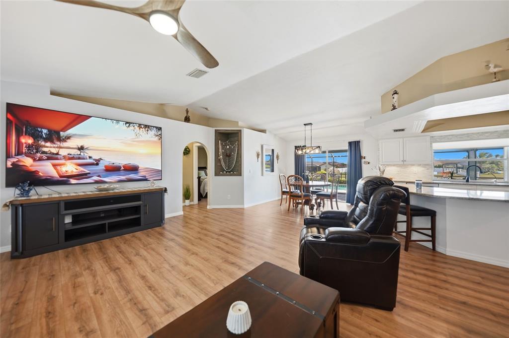 A living room with wood-look flooring, a large television, and an open-concept kitchen area — 515 GLEASON PARKWAY, CAPE CORAL, FL