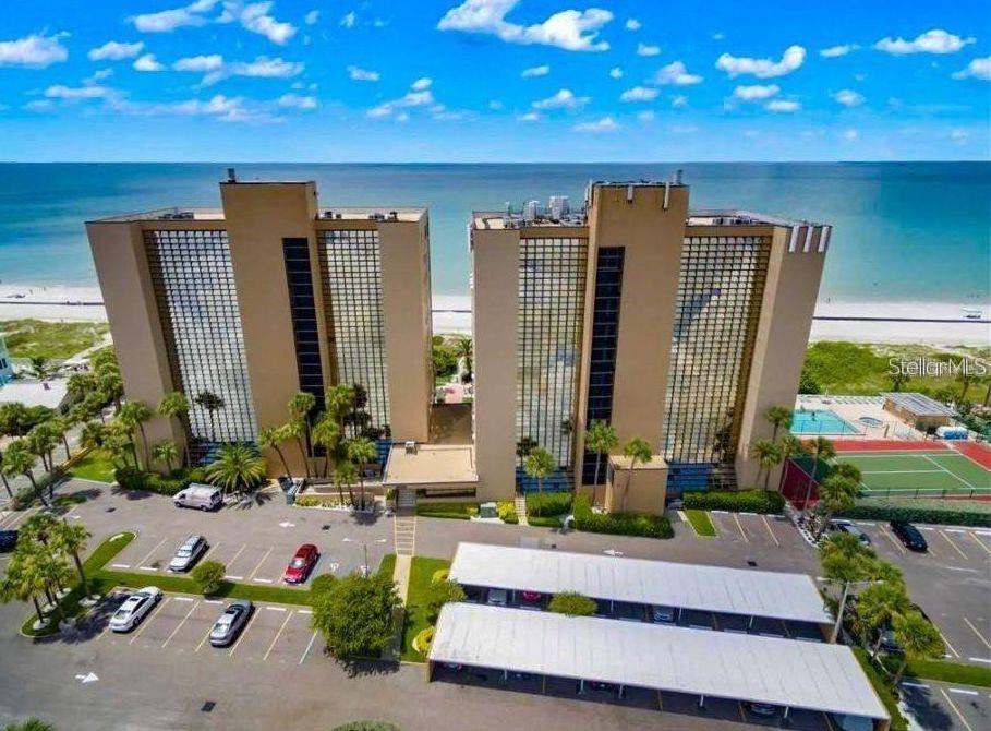 An aerial view of two tall, tan beachfront condominium buildings with a parking lot and tennis court — 900 GULF BOULEVARD UNIT 907, INDIAN ROCKS BEACH, FL