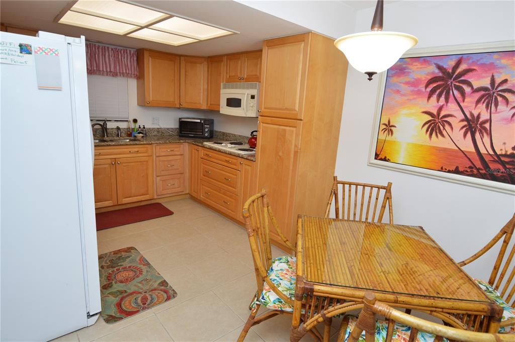 A kitchen with light wood cabinets, granite countertops, and a small dining area with bamboo furniture — 900 GULF BOULEVARD UNIT 907, INDIAN ROCKS BEACH, FL