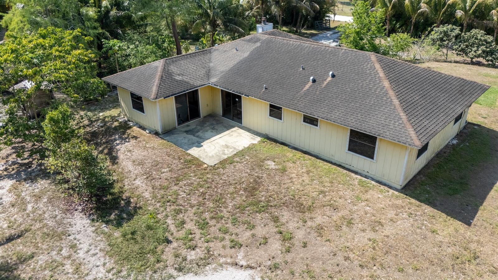 An aerial view shows the back of a yellow house with a concrete patio — 17254 32nd Lane N, FL 33470, FL