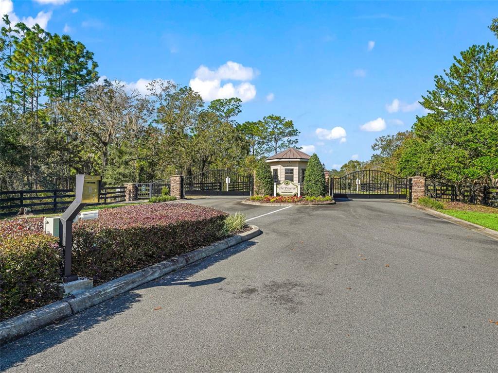 A paved driveway leads to the gated entrance of a residential community with lush landscaping — 2395 NW 81ST AVENUE, WILDWOOD, FL