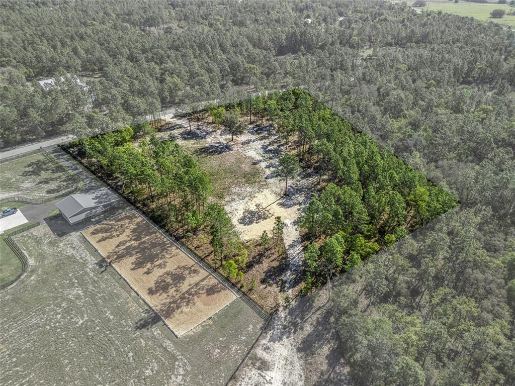 An aerial view shows a rectangular, partially wooded lot adjacent to a fenced riding arena — 2395 NW 81ST AVENUE, WILDWOOD, FL