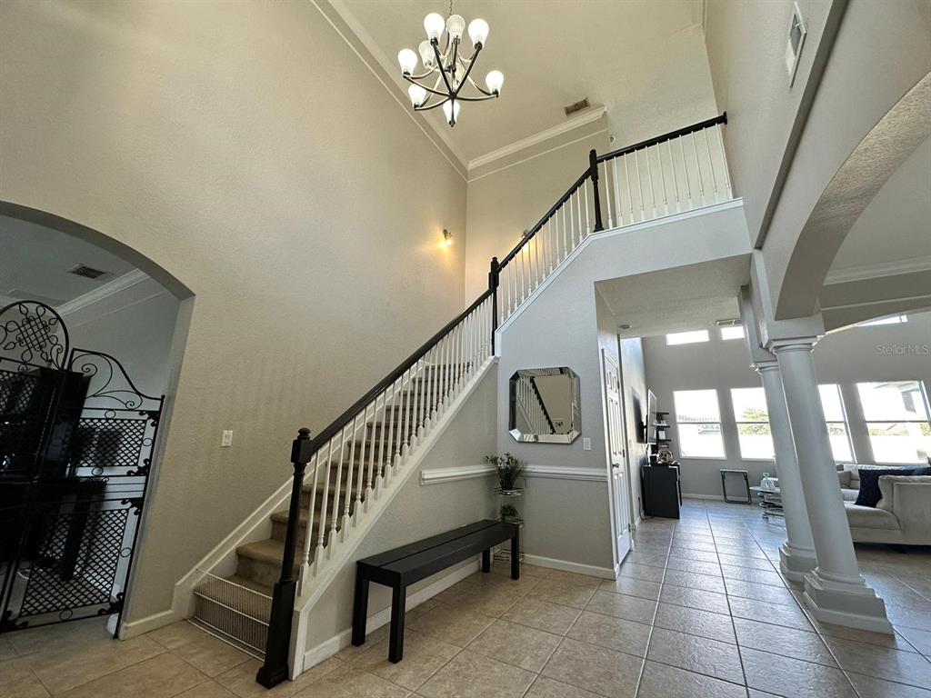 A foyer features a staircase with a black railing, tile flooring, and a chandelier — 2321 HINSDALE DRIVE, KISSIMMEE, FL