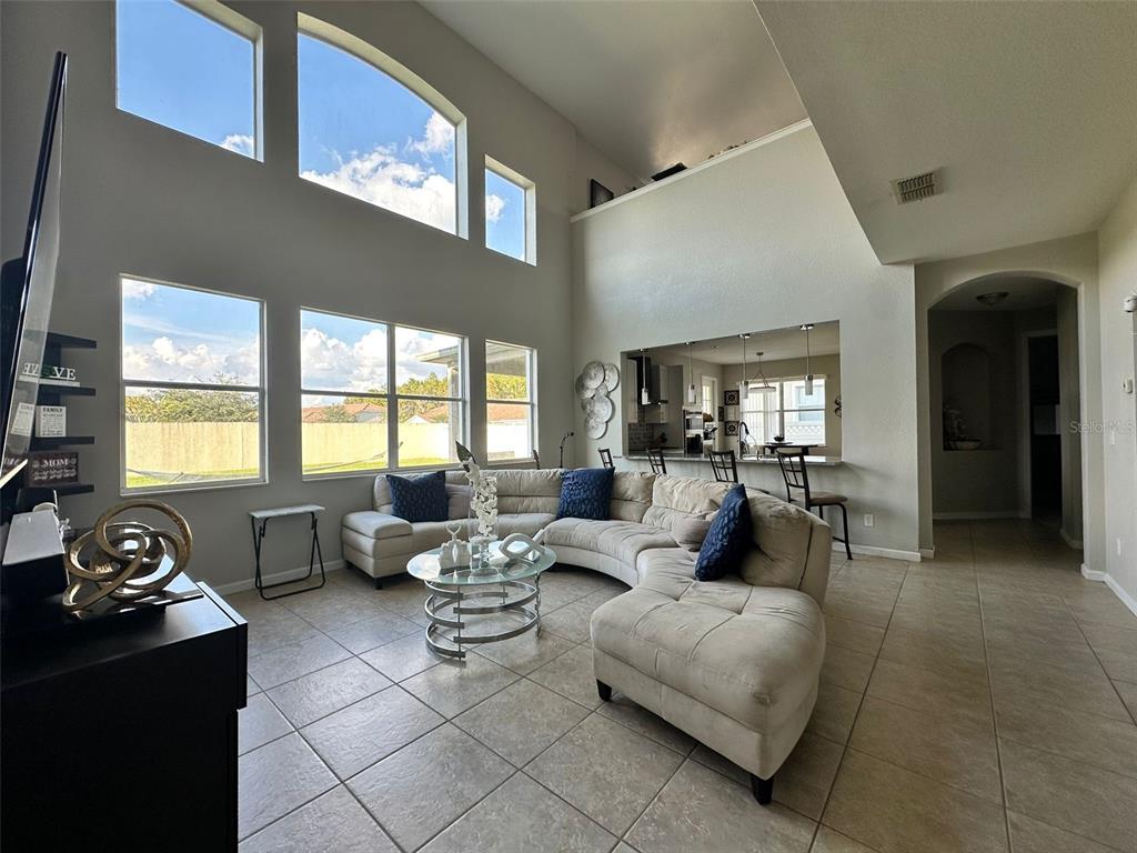 A spacious living room features high ceilings, large windows, tile flooring, and a sectional sofa — 2321 HINSDALE DRIVE, KISSIMMEE, FL