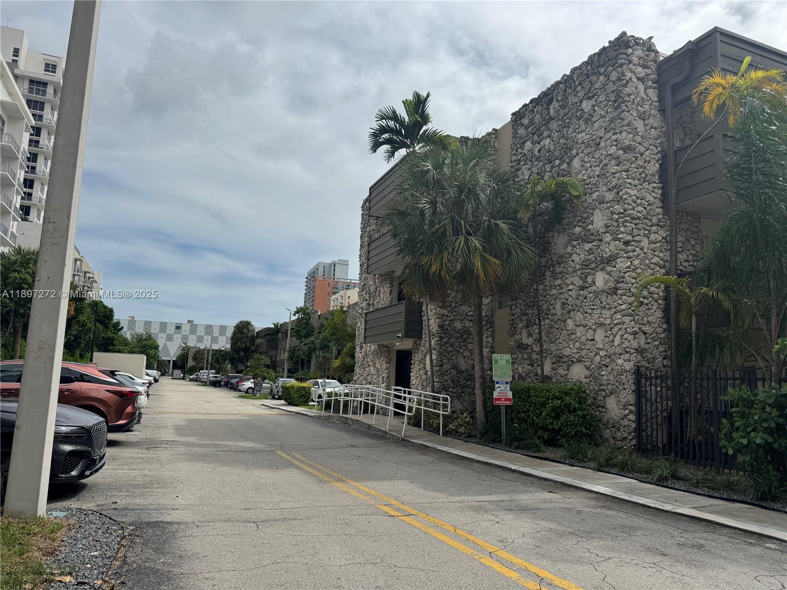 An exterior view of a multi-story building with a textured stone facade and palm trees — 8315 SW 72nd Ave # 101B, Miami FL 33143, MIAMI, FL