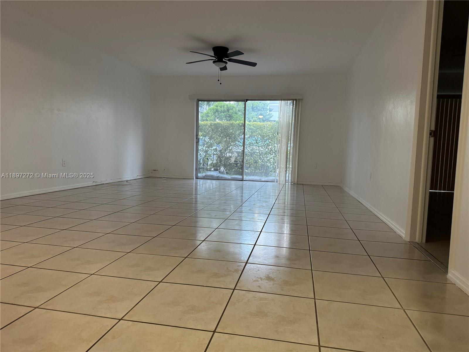 An empty room features white walls, tan tile flooring, a ceiling fan, and sliding doors — 8315 SW 72nd Ave # 101B, Miami FL 33143, MIAMI, FL