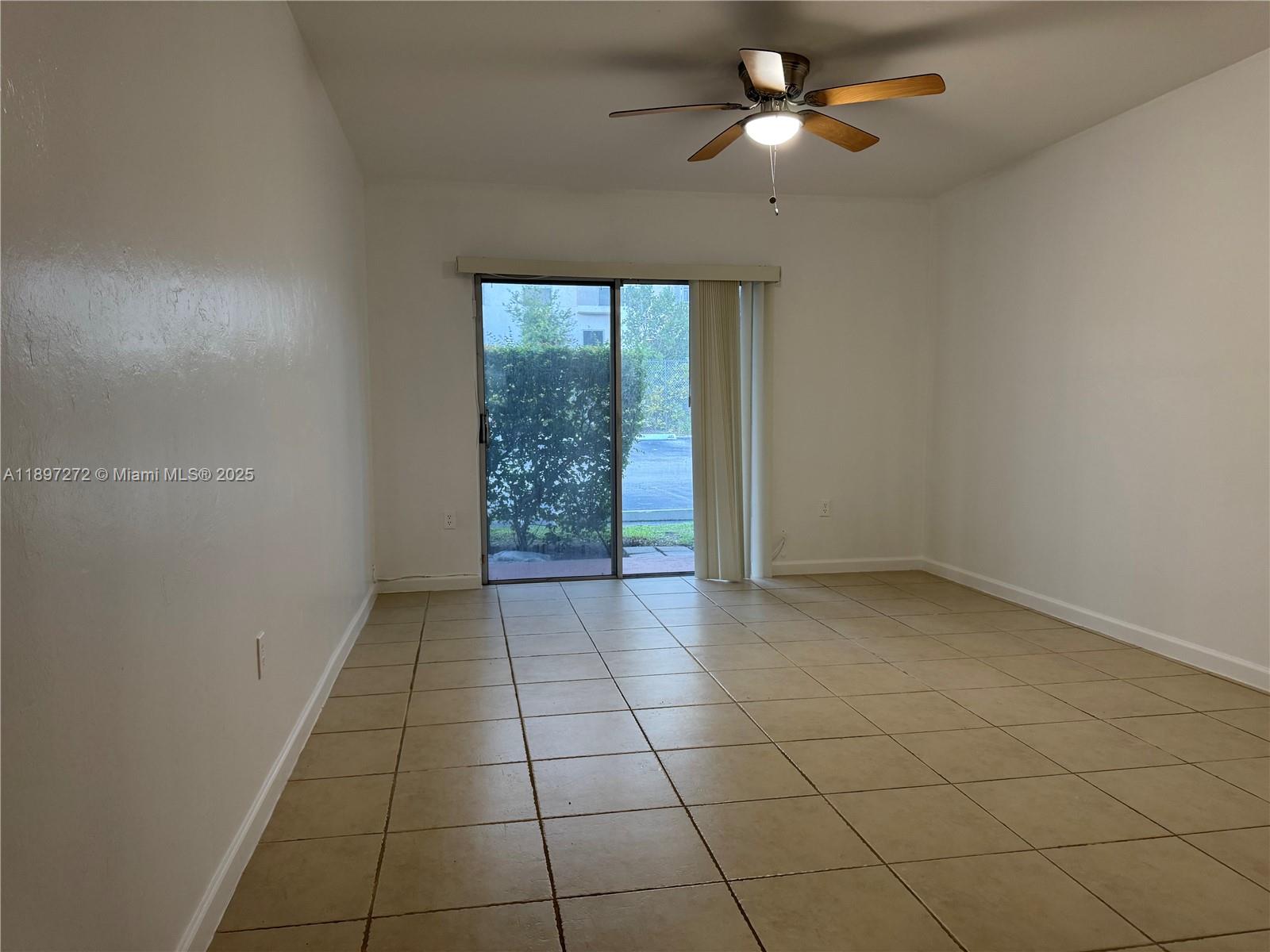 An empty room features beige tile flooring, white walls, a ceiling fan, and sliding glass doors — 8315 SW 72nd Ave # 101B, Miami FL 33143, MIAMI, FL