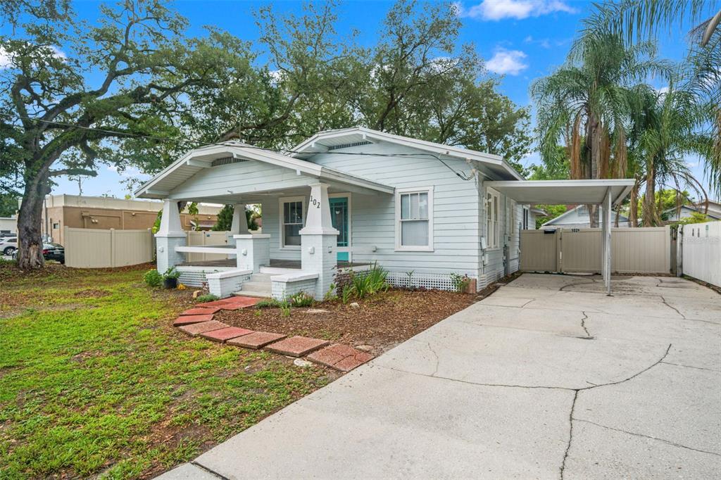 A light blue bungalow with a front porch, carport, and concrete driveway under a blue sky — 102 W NORTH STREET, TAMPA, FL