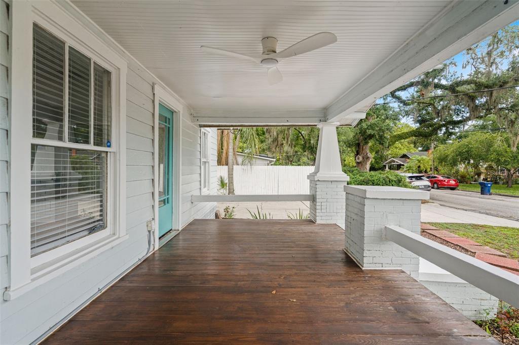 A covered front porch features a dark wood floor, white siding, and a ceiling fan — 102 W NORTH STREET, TAMPA, FL