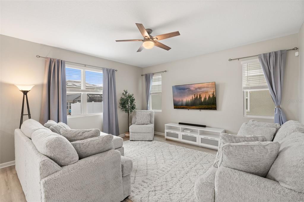 A living room features light gray sofas, a white media console, and a ceiling fan — 1542 SUGARBELLE CIRCLE, MASCOTTE, FL