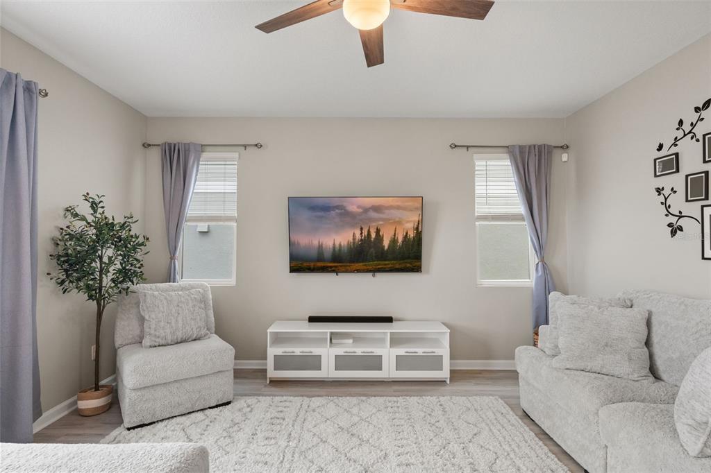 A living room features a wall-mounted television, a white media console, and two windows — 1542 SUGARBELLE CIRCLE, MASCOTTE, FL
