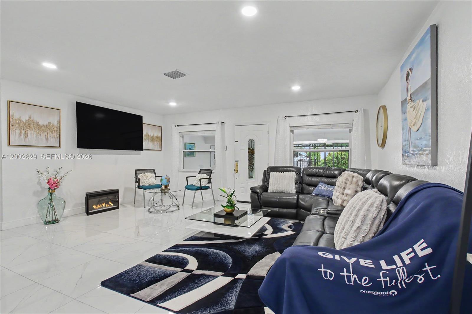 A living room features white tile floors, a black sectional sofa, and a wall-mounted television — 2145 NW 133rd St # 2145, Miami FL 33167, MIAMI, FL