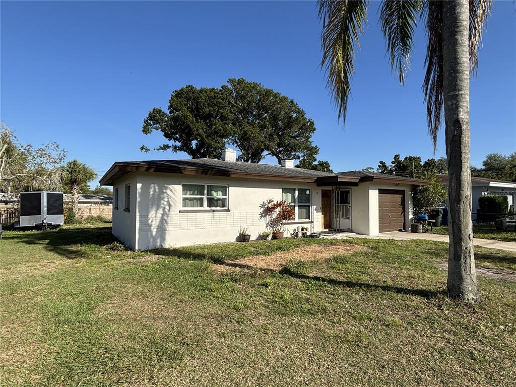 A single-story house with a light-colored exterior, a brown garage door, and a palm tree — 1347 BUCKINGHAM DRIVE, CLEARWATER, FL
