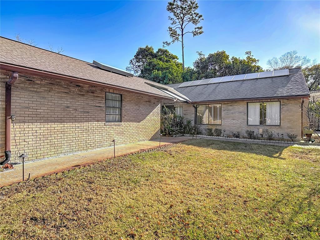A brick house exterior features a paved walkway, a grassy yard, and solar roof panels — 65 ELMWOOD TRAIL, DELAND, FL