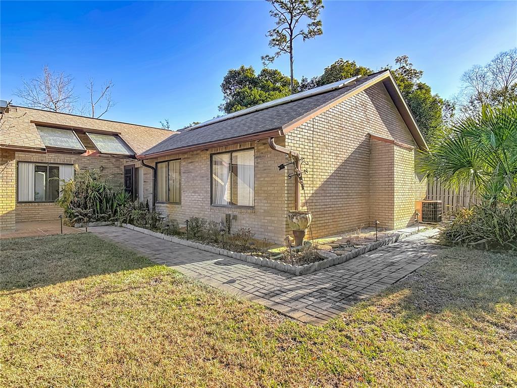 A brick house exterior features a paved walkway, skylights, and a small garden area — 65 ELMWOOD TRAIL, DELAND, FL