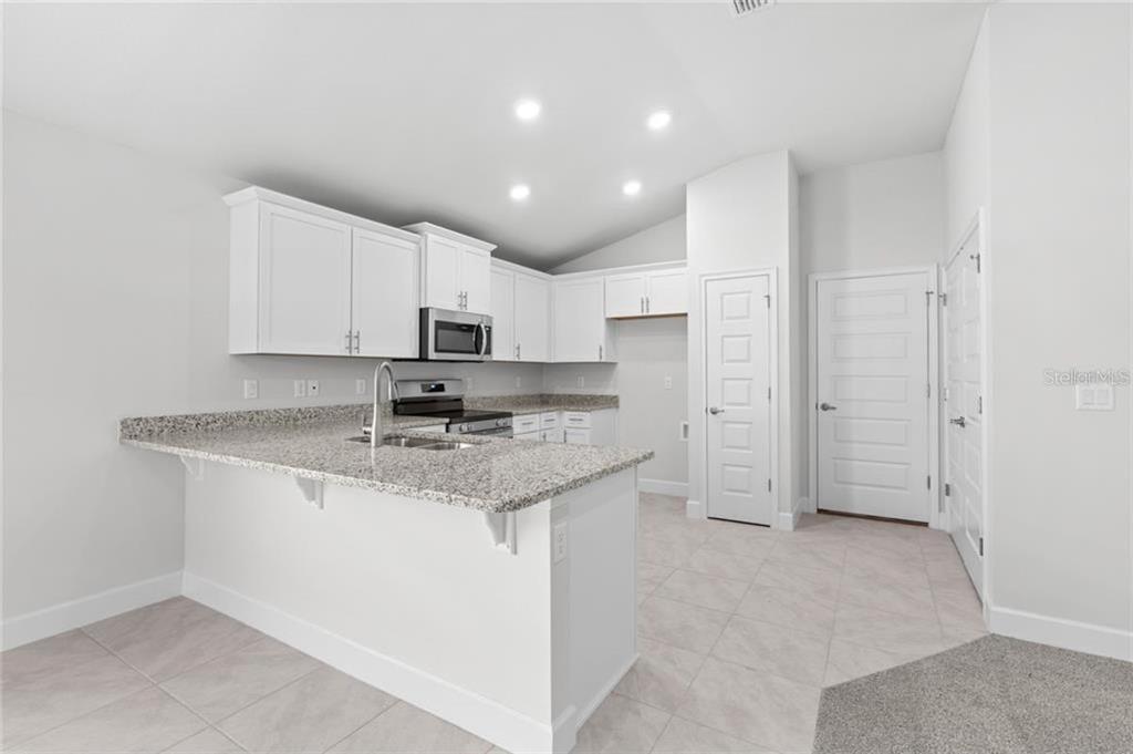 A kitchen features white cabinets, granite countertops, a breakfast bar, and light-colored tile flooring — 19 SEDGEFIELD PATH S, PALM COAST, FL
