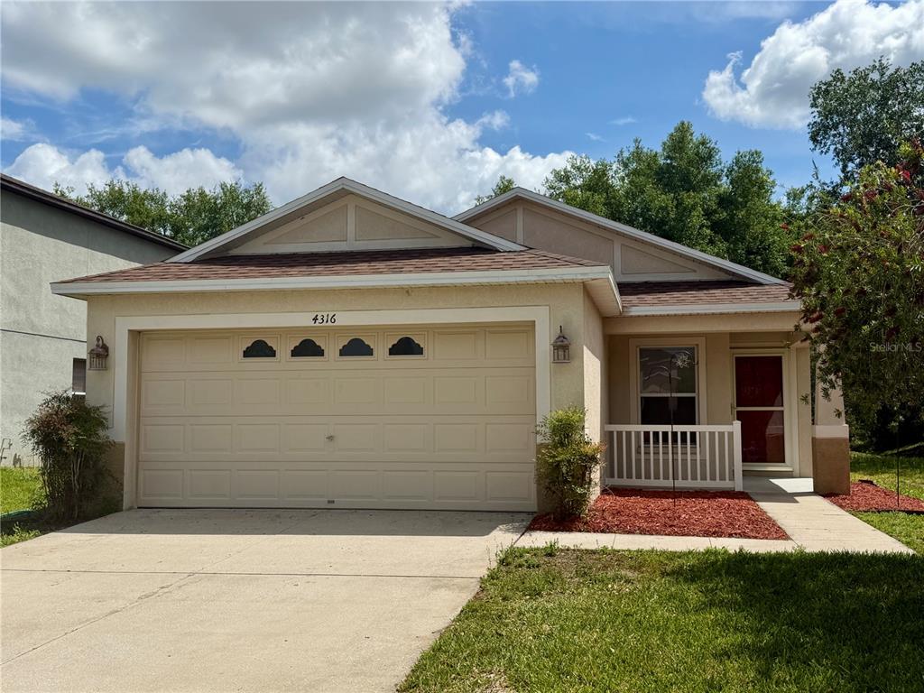 A single-story house with a beige stucco exterior, a two-car garage, and a front porch — 4316 OLD WAVERLY COURT, WESLEY CHAPEL, FL