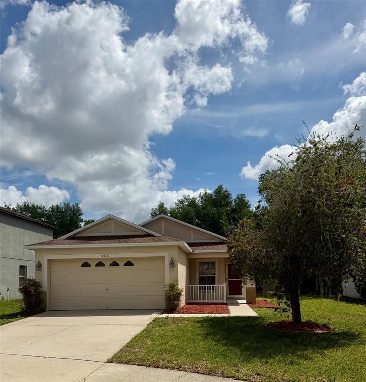 A single-story house with a beige garage, a small front porch, and a large tree — 4316 OLD WAVERLY COURT, WESLEY CHAPEL, FL