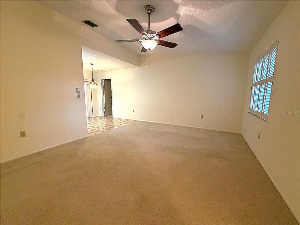An empty living room features beige carpeting, a ceiling fan, and a window with shutters — 6736 JARVIS ROAD, SARASOTA, FL