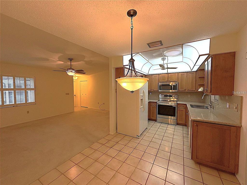 A kitchen with wood cabinets and tile floors opens to a carpeted living area — 6736 JARVIS ROAD, SARASOTA, FL