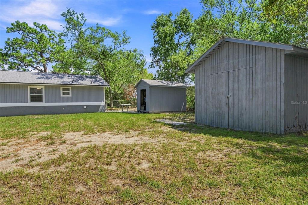 A backyard features a grey house, two storage sheds, and a patch of grass — 10380 GOLDEN AVENUE, WEEKI WACHEE, FL