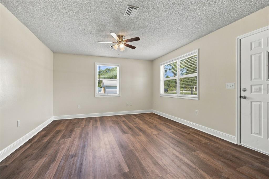 An empty room features light-colored walls, wood-look flooring, a ceiling fan, and two windows — 10380 GOLDEN AVENUE, WEEKI WACHEE, FL