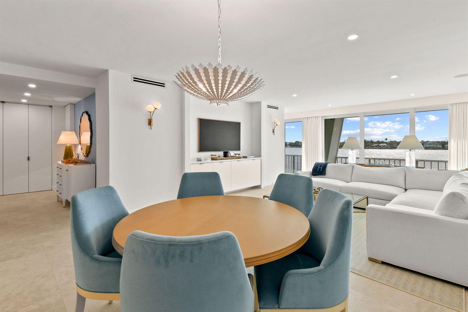 A dining area with a round wooden table and blue chairs opens to a living room — 2180 Ibis Isle Road # 12, Palm Beach FL 33480, PALM BEACH, FL