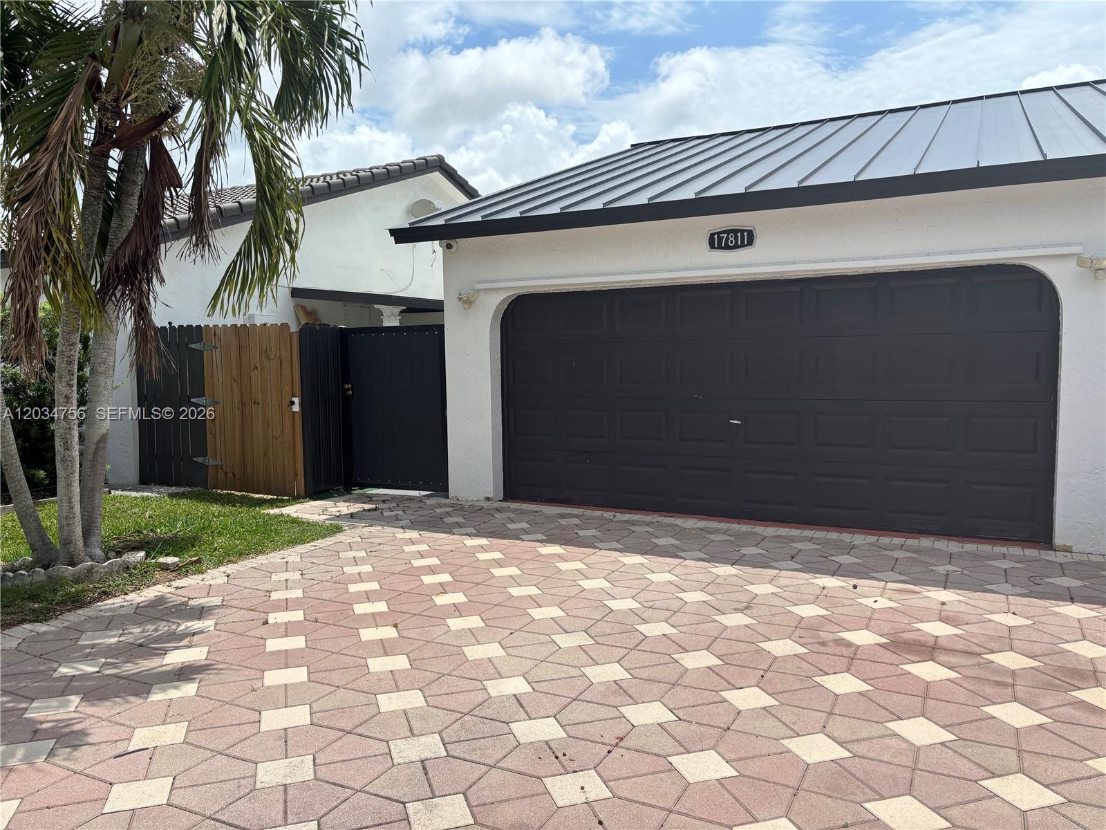 A white house with a dark metal roof and a paved driveway featuring a garage — 17811 SW 152nd Pl, Miami FL 33187, MIAMI, FL