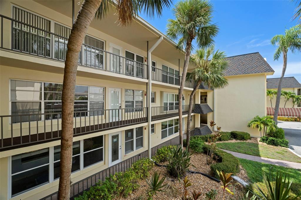 Exterior view of a three-story apartment building with balconies and palm trees in the foreground — 4780 COVE CIRCLE UNIT 205, ST PETERSBURG, FL