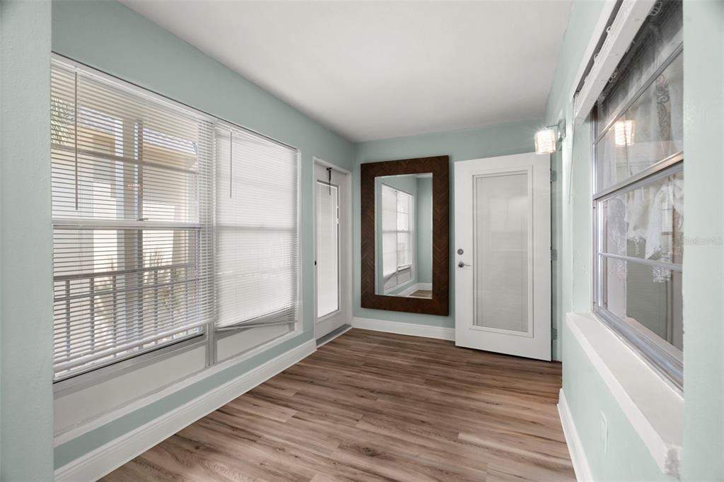A sunroom with light blue walls, wood-look flooring, a large mirror, and two glass doors — 4780 COVE CIRCLE UNIT 205, ST PETERSBURG, FL