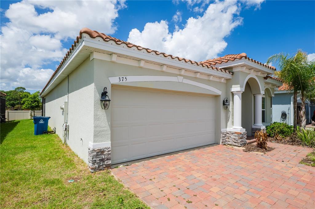 A single-story house exterior features a two-car garage, a brick paver driveway, and tile roofing — 375 VILLA SORRENTO CIRCLE, HAINES CITY, FL