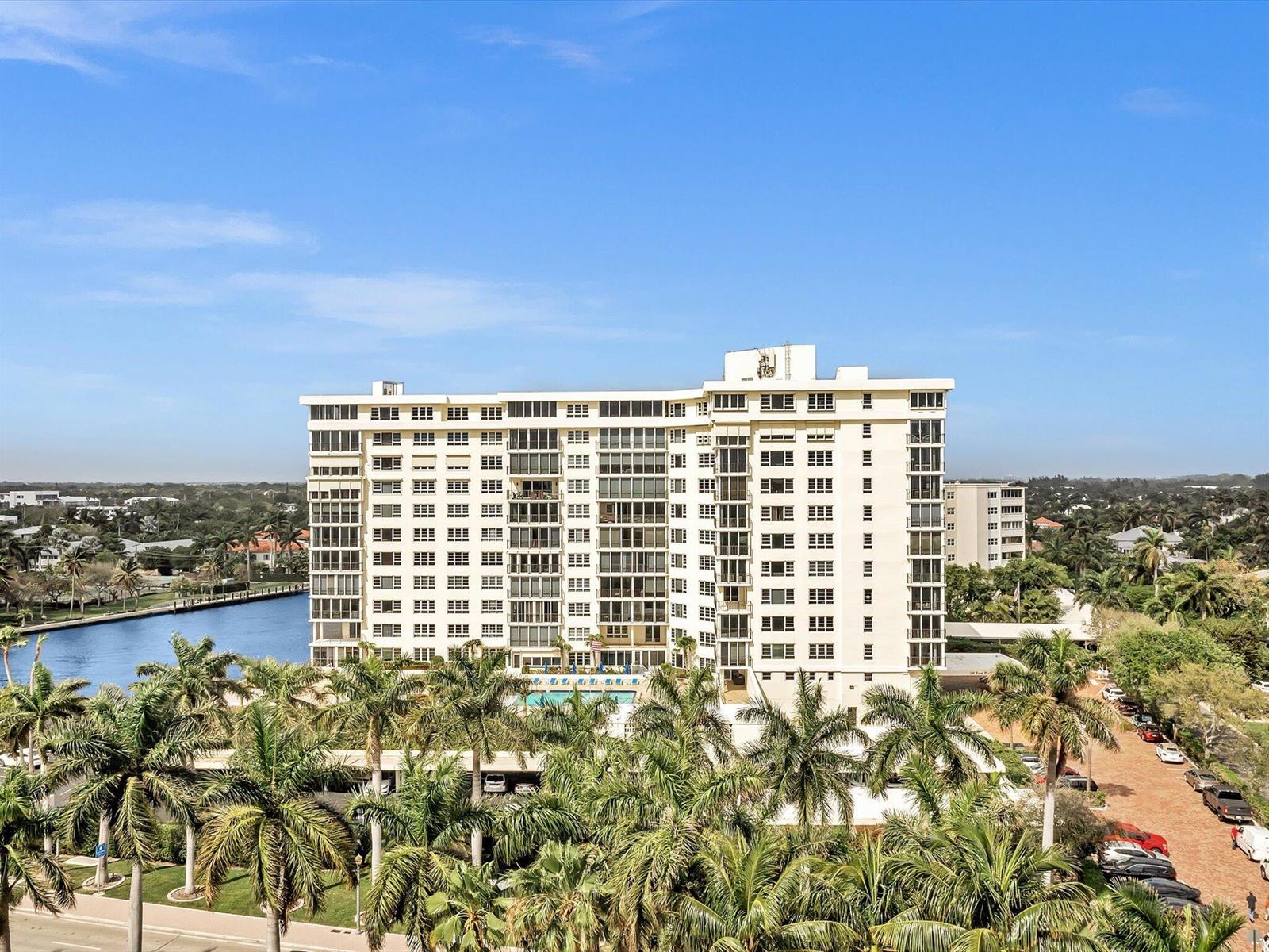 An aerial view shows a multi-story apartment building surrounded by palm trees and a canal — 50 East Road # 12f, Delray Beach FL 33483, DELRAY BEACH, FL