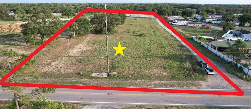 An aerial view shows a large, vacant, trapezoidal grassy lot bordered by a road and fences — 5645 JOHNSON AVENUE E, HAINES CITY, FL