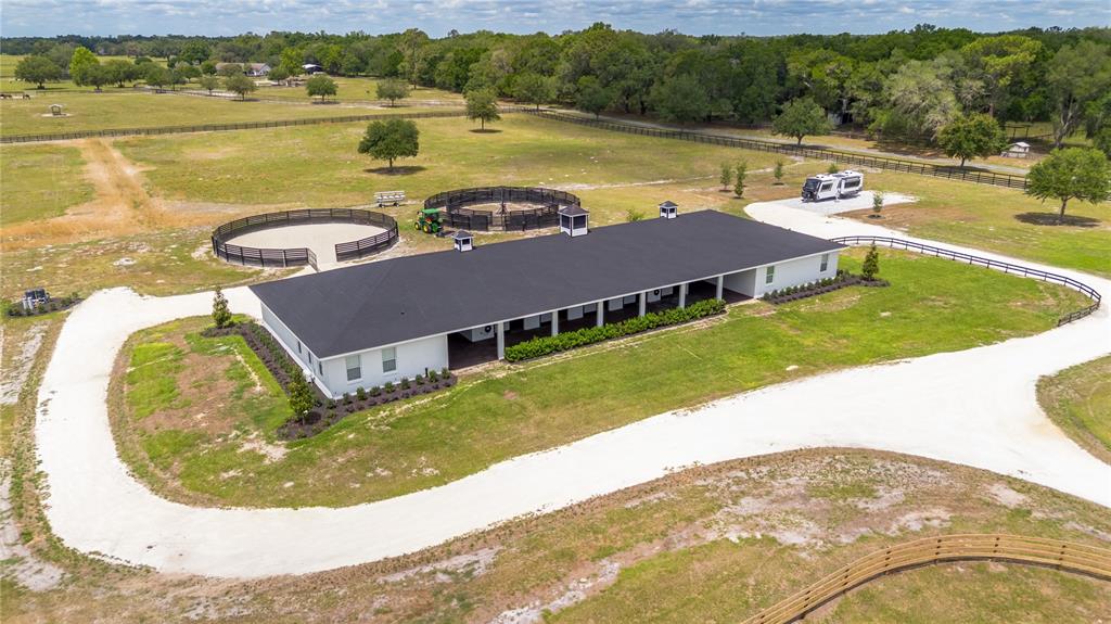 An aerial view shows a white horse barn with a black roof and two round pens — 6170 NW 135TH AVENUE, MORRISTON, FL