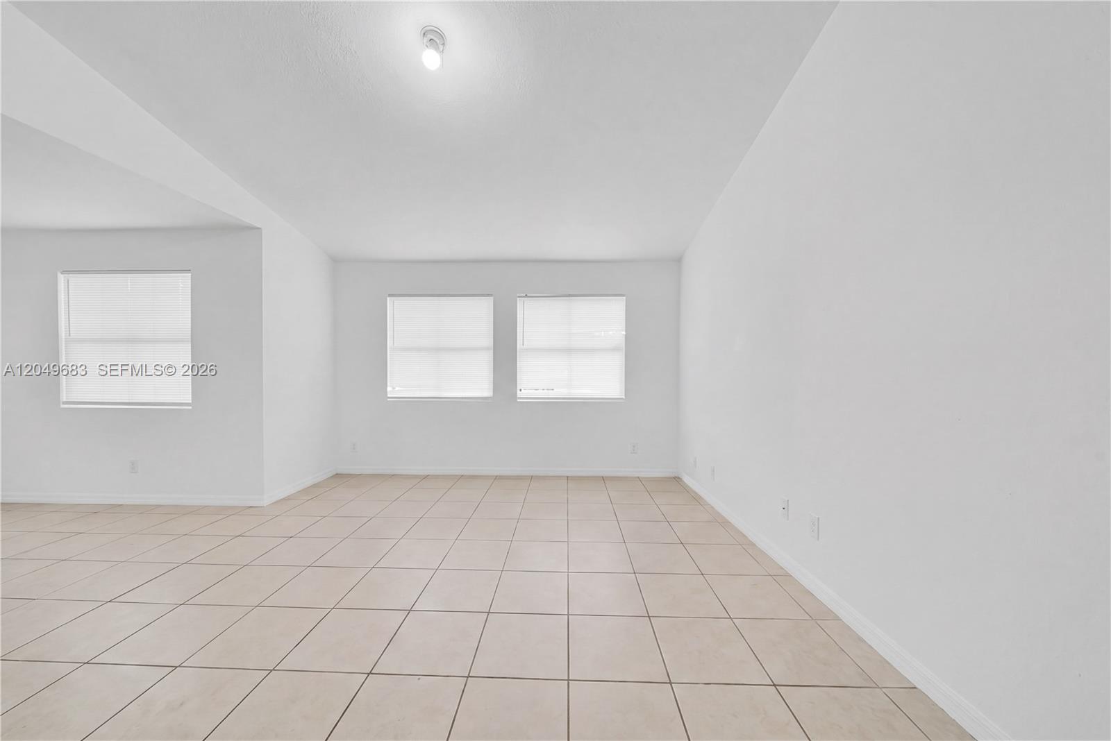 An empty room features white walls, beige tile flooring, and three windows with blinds — 15070 SW 103rd Ln # 2201, Miami FL 33196, MIAMI, FL