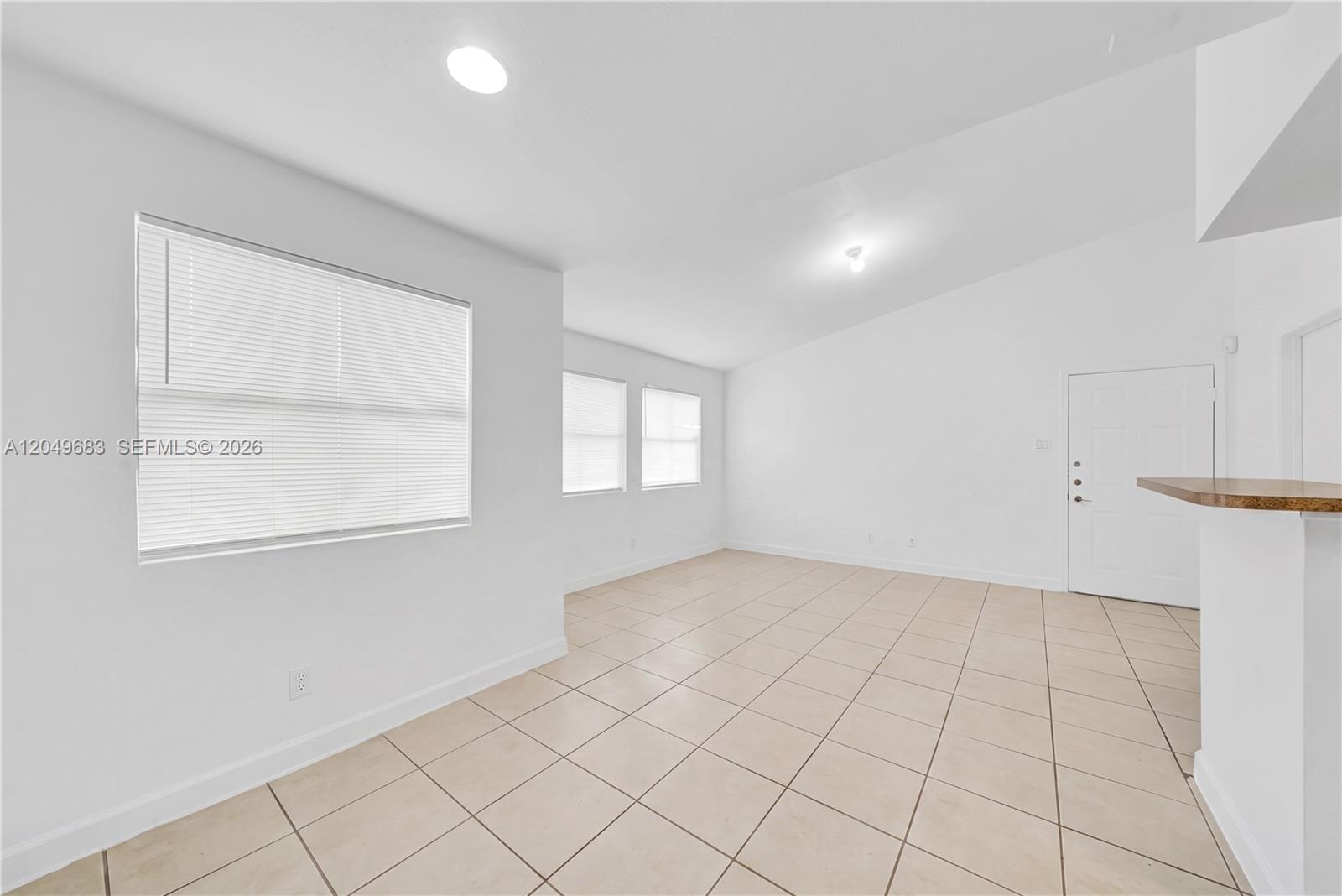 An empty room features white walls, beige tile flooring, and several windows with blinds — 15070 SW 103rd Ln # 2201, Miami FL 33196, MIAMI, FL