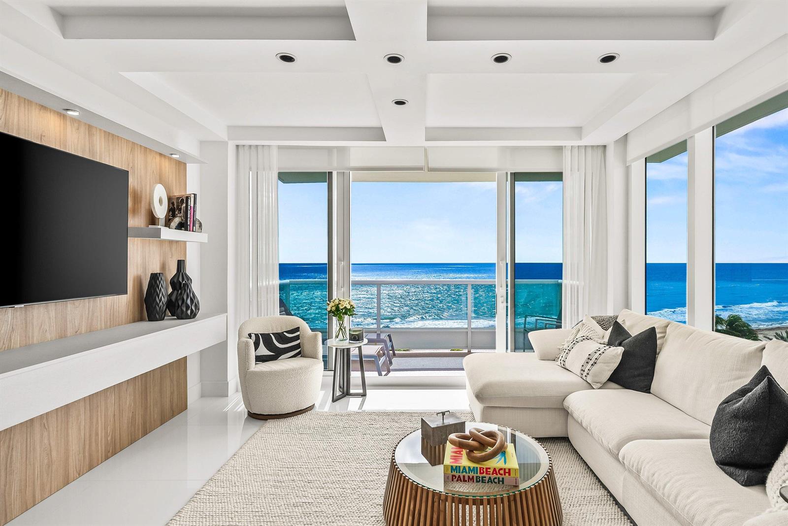 A modern living room features a sectional sofa, wood-paneled wall, and floor-to-ceiling ocean views — 700 S Ocean Boulevard # 705, Boca Raton FL 33432, BOCA RATON, FL