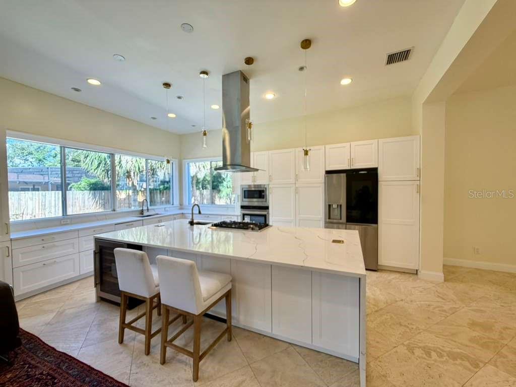 A modern kitchen features a large white quartz island, white cabinetry, and stainless steel appliances — 672 MOSSY BRANCH COURT, LONGWOOD, FL