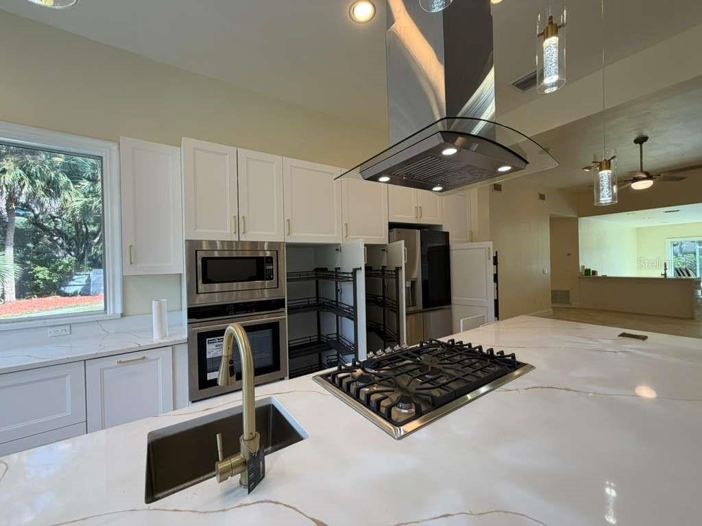 A modern kitchen features white cabinets, a large quartz island with a gas cooktop, and stainless appliances — 672 MOSSY BRANCH COURT, LONGWOOD, FL