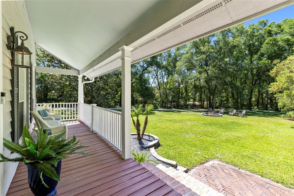 A covered wooden porch overlooks a grassy backyard with a fire pit and trees — 5787 N APOPKA VINELAND ROAD, ORLANDO, FL