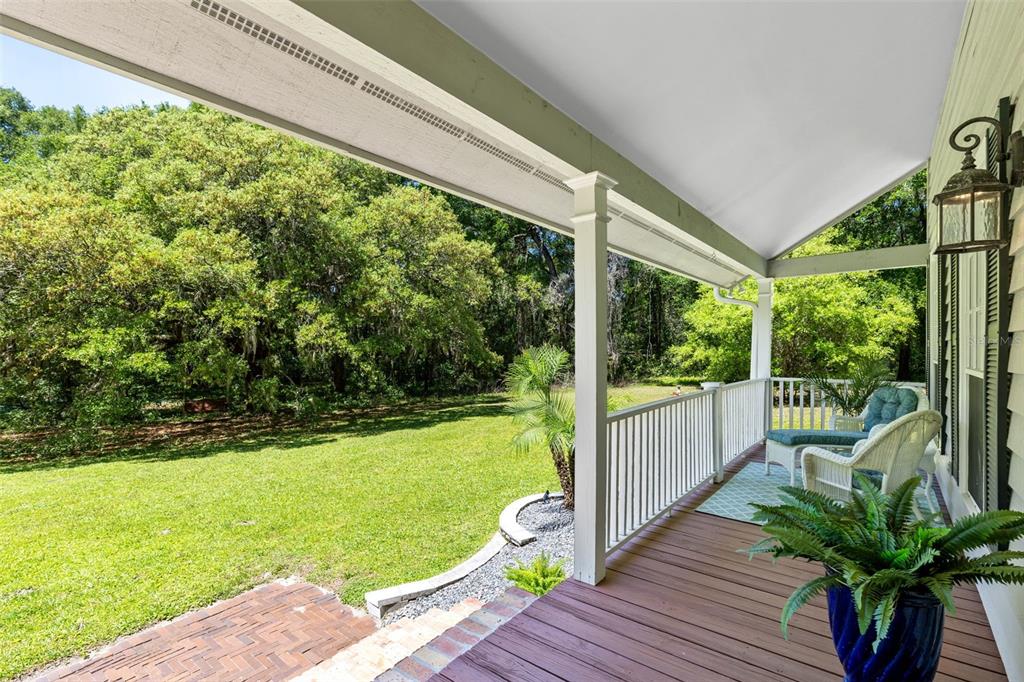 A covered wooden porch overlooks a grassy backyard with mature trees and a brick patio — 5787 N APOPKA VINELAND ROAD, ORLANDO, FL