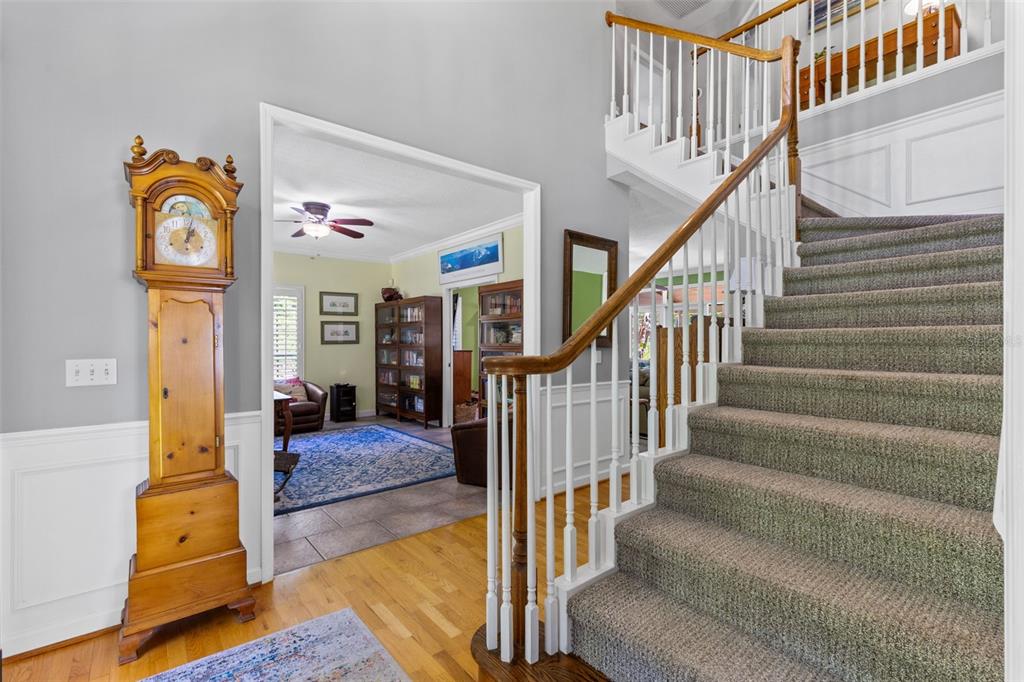 A grand staircase with carpeted steps stands beside a tall wooden grandfather clock — 5787 N APOPKA VINELAND ROAD, ORLANDO, FL