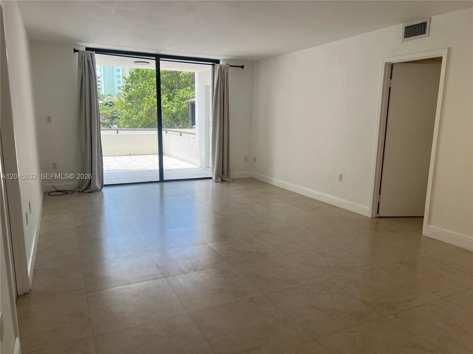 An empty room features large beige floor tiles, white walls, and a sliding glass door — 2333 Brickell Ave # 210, Miami FL 33129, MIAMI, FL