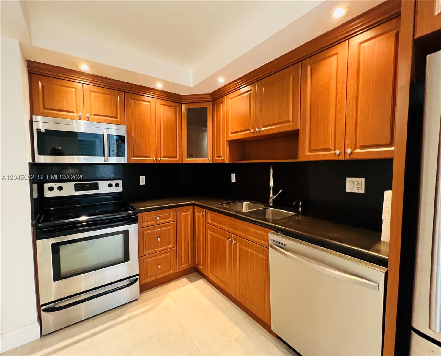 A kitchen features wood cabinets, stainless steel appliances, and black countertops — 2333 Brickell Ave # 210, Miami FL 33129, MIAMI, FL