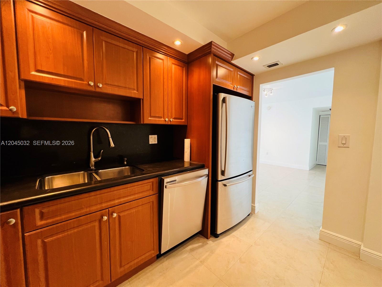 A kitchen features wood cabinets, stainless steel appliances, and a black countertop — 2333 Brickell Ave # 210, Miami FL 33129, MIAMI, FL