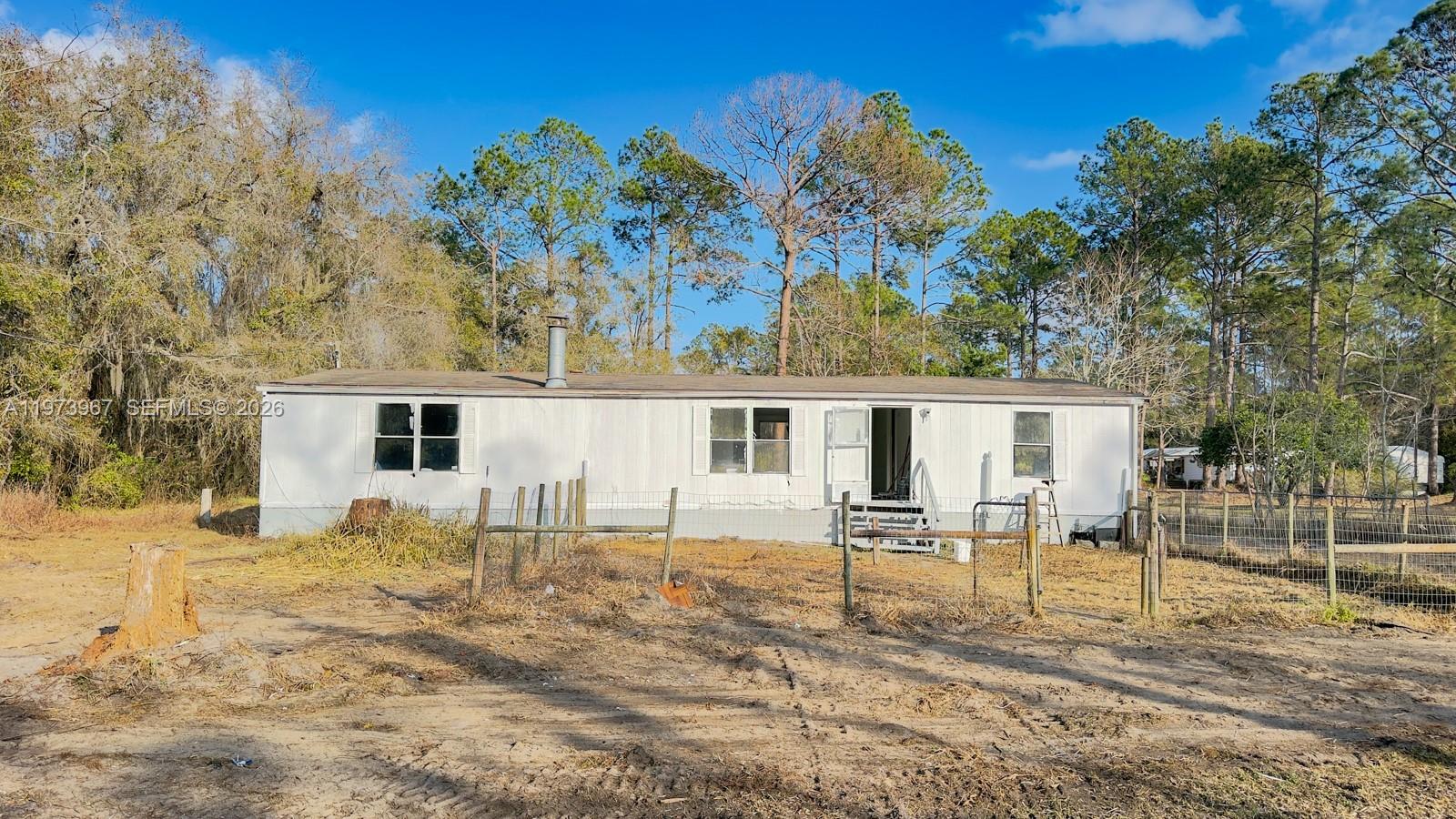 A single-story mobile home sits on a dirt lot surrounded by trees and fencing — 124 Cypress Dr, Palatka FL 32177, PALATKA, FL