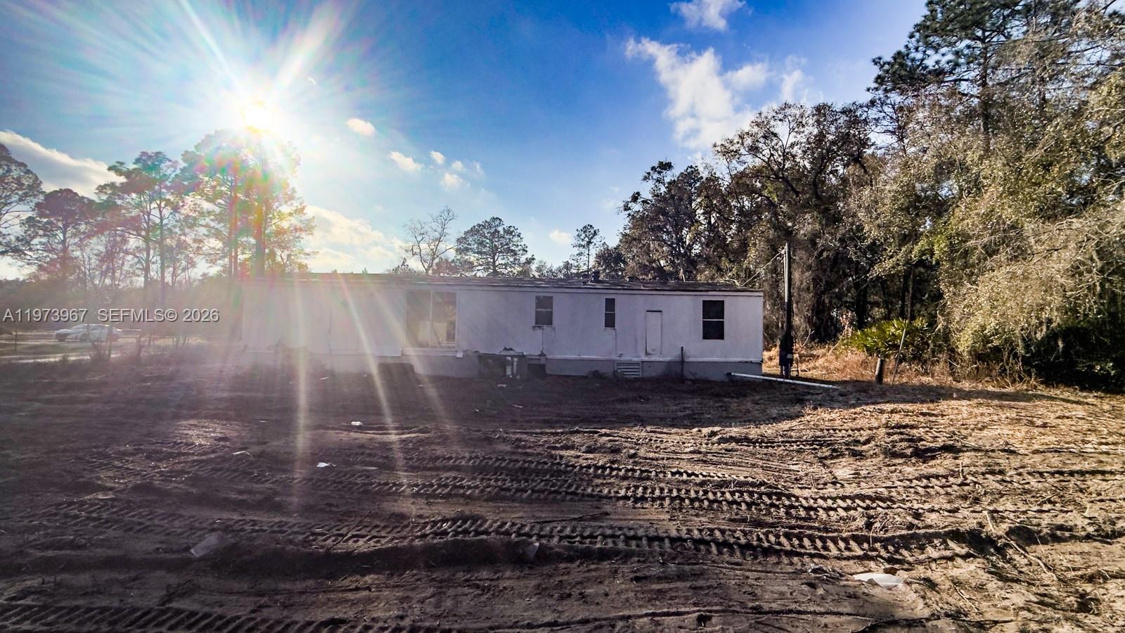A single-story mobile home sits on a cleared, dirt lot under a bright sun — 124 Cypress Dr, Palatka FL 32177, PALATKA, FL