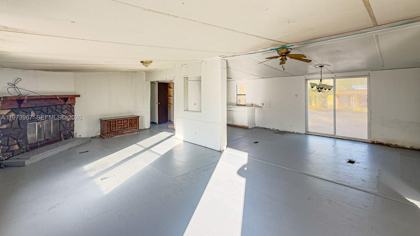 An open-concept living room features a stone fireplace, gray painted floors, and a kitchen area — 124 Cypress Dr, Palatka FL 32177, PALATKA, FL